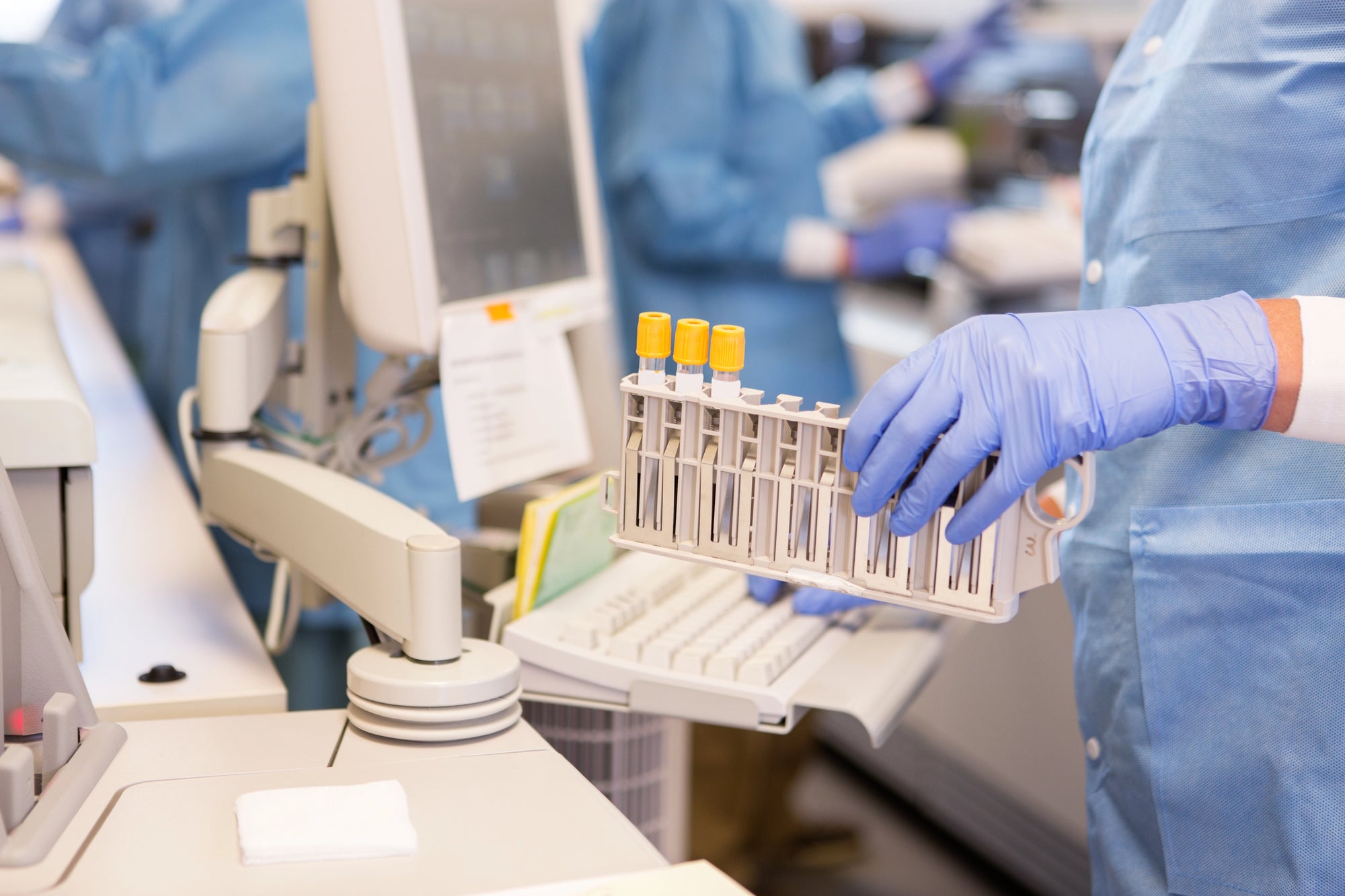 Person in a laboratory setting holding test tubes with a computer in the background